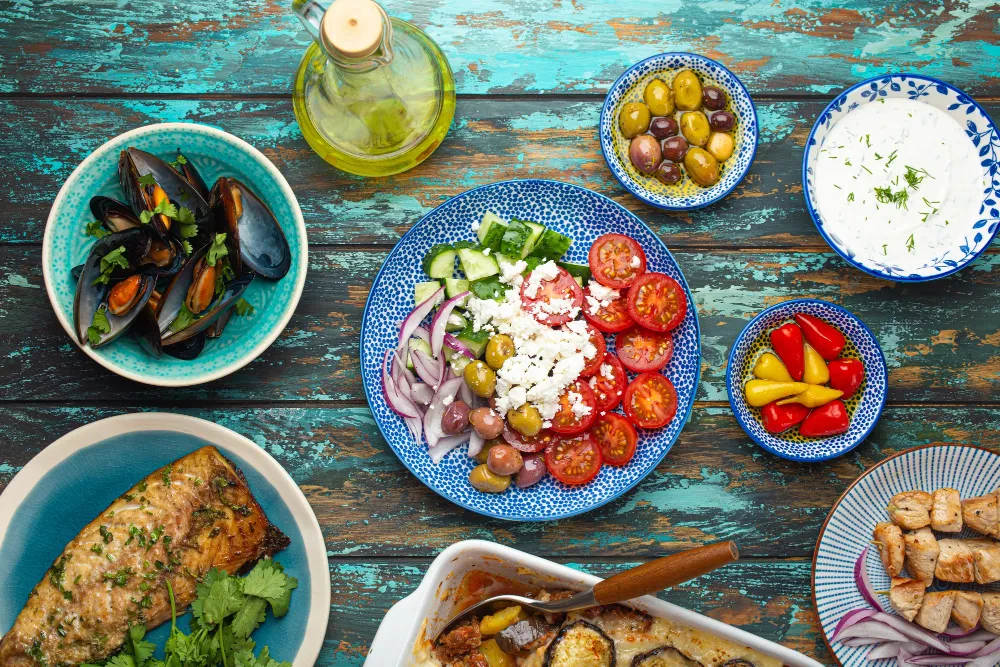 Assorted Greek dishes on rustic wooden background from above, moussaka, grilled fish, souvlaki, greek salad, steamed mussels with herbs, appetizers of Greece from above
